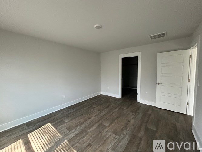 A room with wooden flooring and white walls, with a door on the right side.