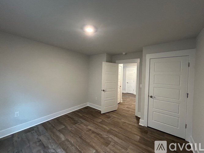 A room with white walls and wooden flooring with three doors.