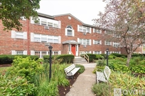 A brick building with a red door and windows, surrounded by greenery and a walkway.