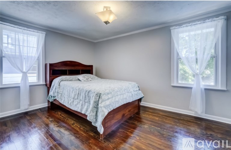 A bedroom with a bed, wooden floors, and two windows with curtains.