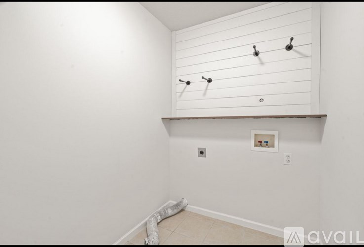 A white wall with four black hooks and a small picture frame.