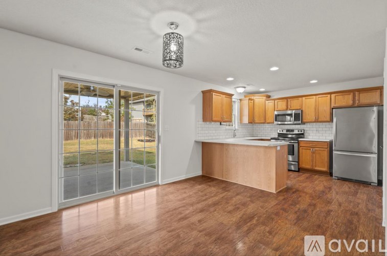 A kitchen with wooden floors and a large window with a view of a fence and grass.
