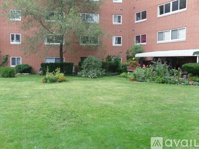A grassy area in front of a red brick building with a tree and bushes.