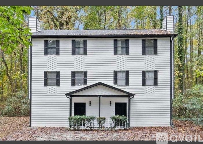 A white house with black shutters is surrounded by trees.