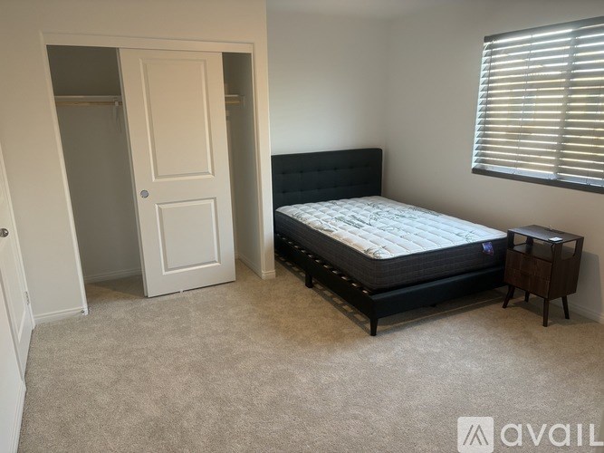 A bedroom with a bed, nightstand, and window with blinds.
