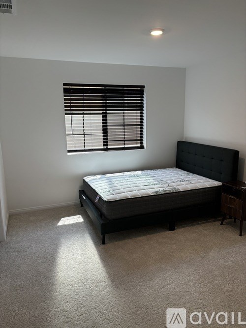 A bedroom with a bed, nightstand, and window with blinds.