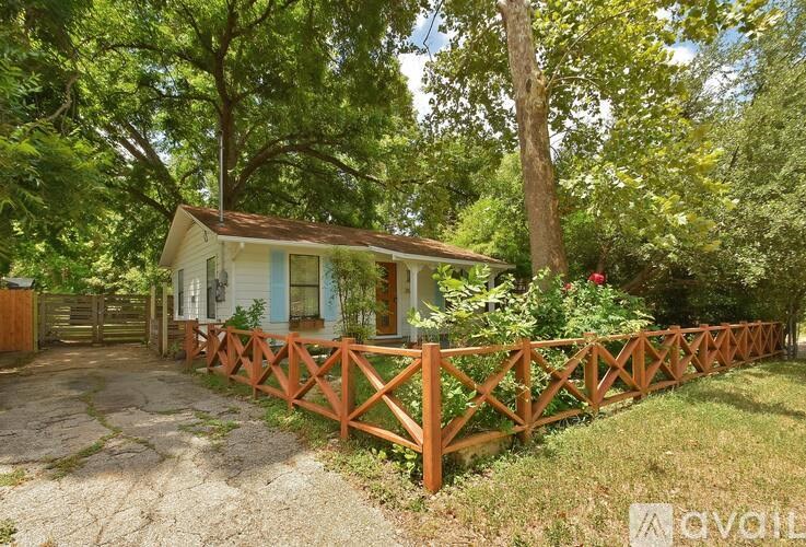 A small house with a porch and a wooden fence is surrounded by greenery.