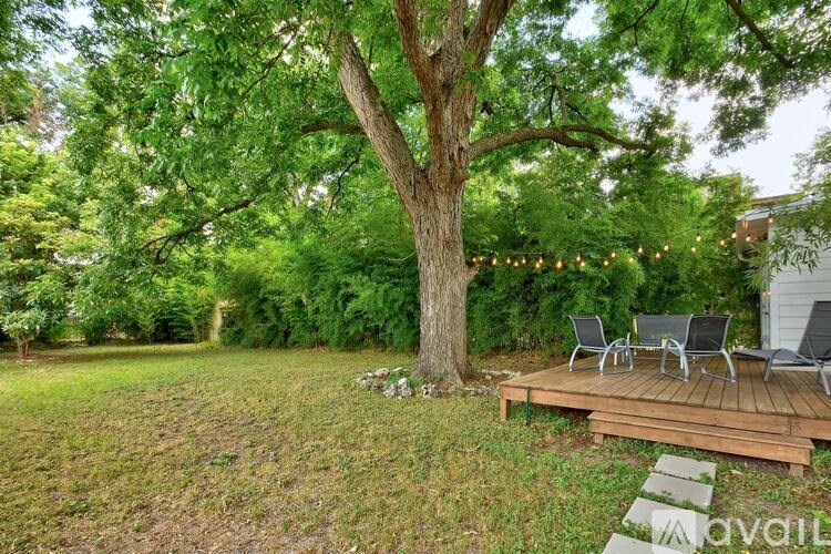 A tree with a wooden deck and chairs in front of it.