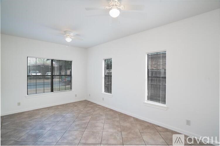 A spacious room with a ceiling fan and two windows.