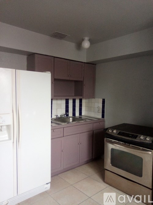 A kitchen with a white fridge, brown oven, and pink cabinets.
