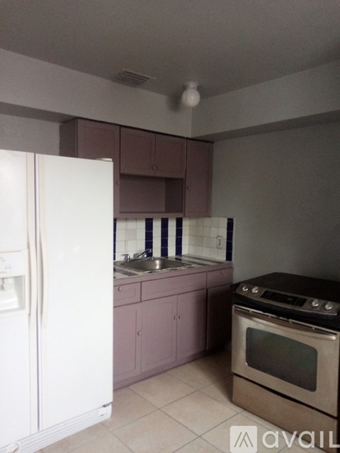 A kitchen with a white fridge, brown oven, and pink cabinets.