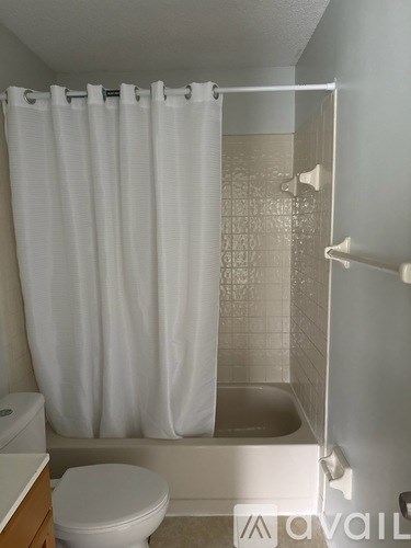 A white toilet sits next to a white shower curtain in a bathroom.