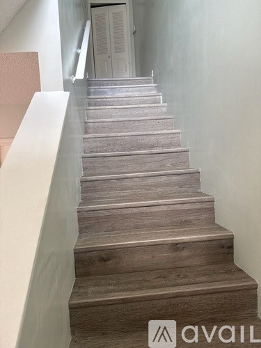 A flight of wooden stairs with a white handrail on the left side.