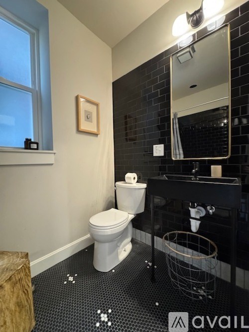 A bathroom with a toilet, a mirror, and a black tiled wall.