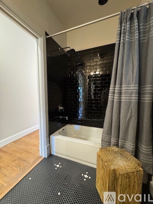 A bathroom with a black tiled shower area and a wooden stool.