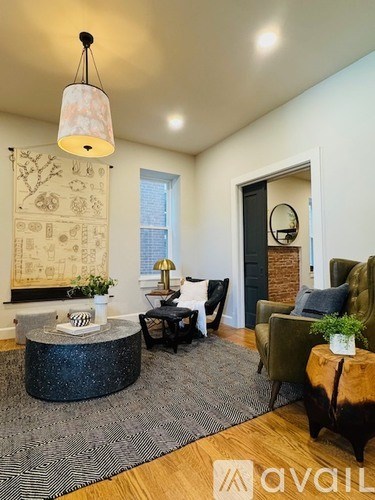 A living room with a black and white rug, a round table with a vase of flowers, a black chair, a green armchair, and a mirror on the wall.