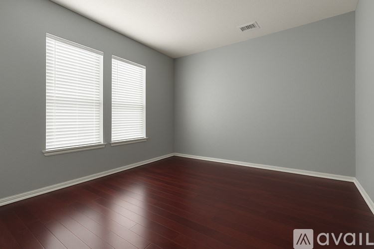 A room with wooden flooring and two windows with blinds.