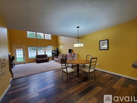 A living room with a brown sofa, a wooden table and chairs, and a rug.