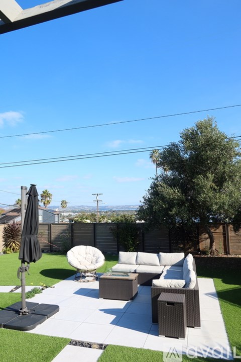 A patio with a black umbrella and white furniture.