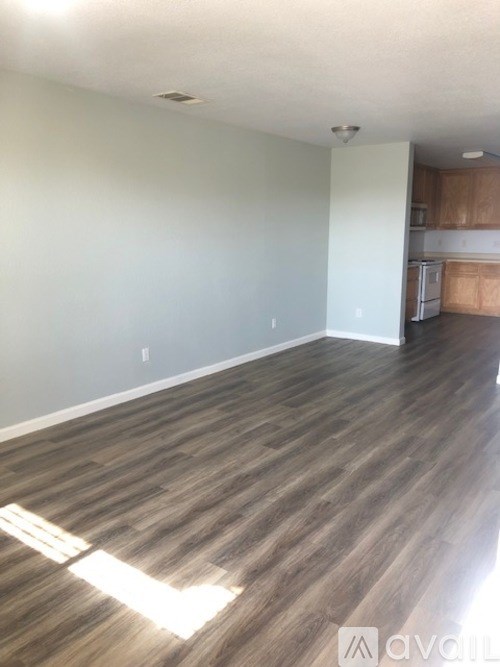 A room with wooden flooring and a kitchen in the background.