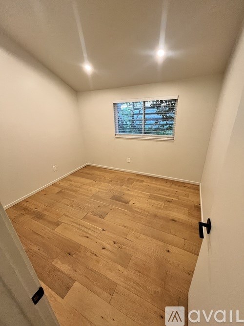 A room with wooden flooring and a window showing trees outside.