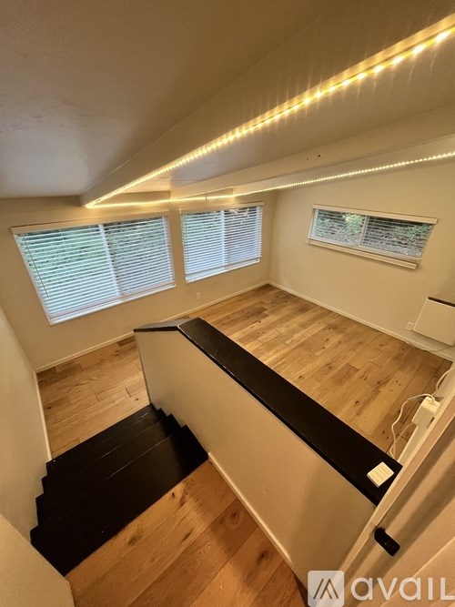 A staircase with a black handrail and wooden steps leads to a room with a window and a wall-mounted air conditioner.