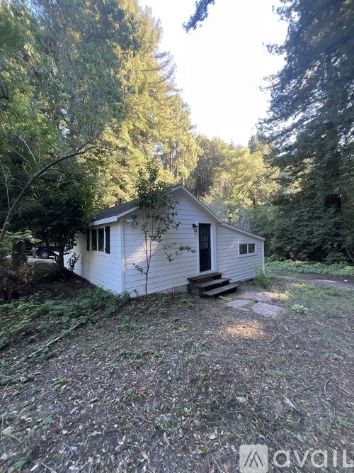 A small white house is surrounded by trees and grass.