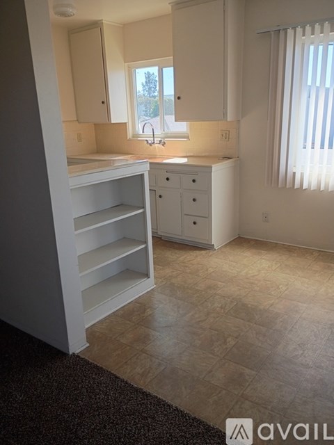 A kitchen with white cabinets and a window with blinds.