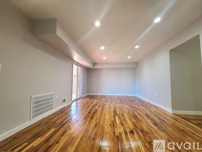 A spacious room with wooden flooring and a large window.
