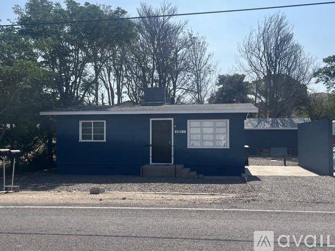 A blue house with a white door and windows is surrounded by trees.