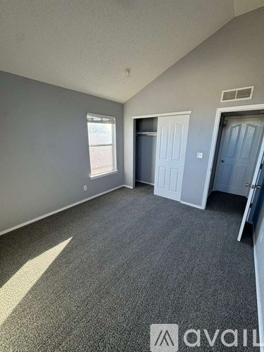 A room with grey carpet and white walls, with a window and a door.