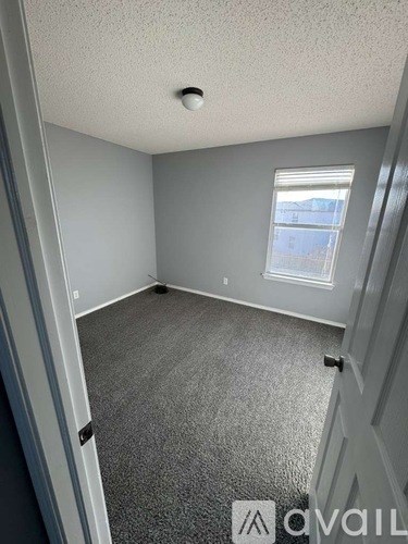A room with grey carpeting and a window.