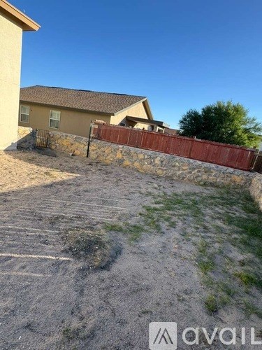A backyard with a stone wall and a house in the background.