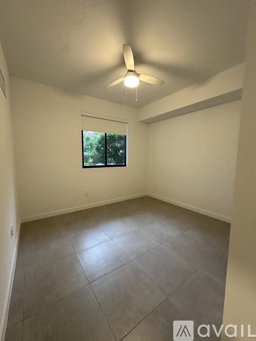 A room with a ceiling fan and a window showing trees outside.