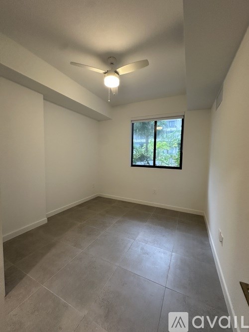 A room with a ceiling fan and a window showing greenery outside.