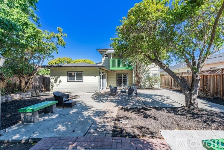 A house with a green roof and a backyard with a bench and a tree.