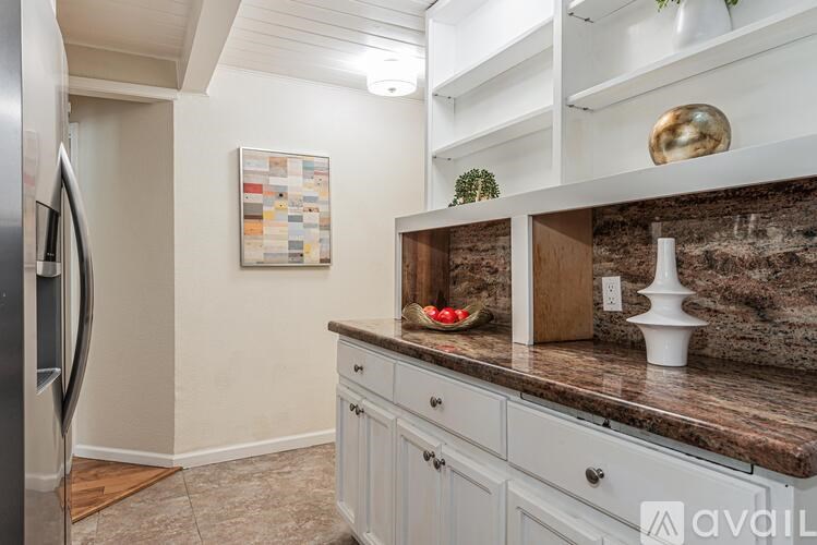 A kitchen with a refrigerator on the left and a counter with a bowl and a vase on it.