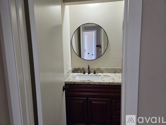 A bathroom with a round mirror, sink, and dark wood cabinet.