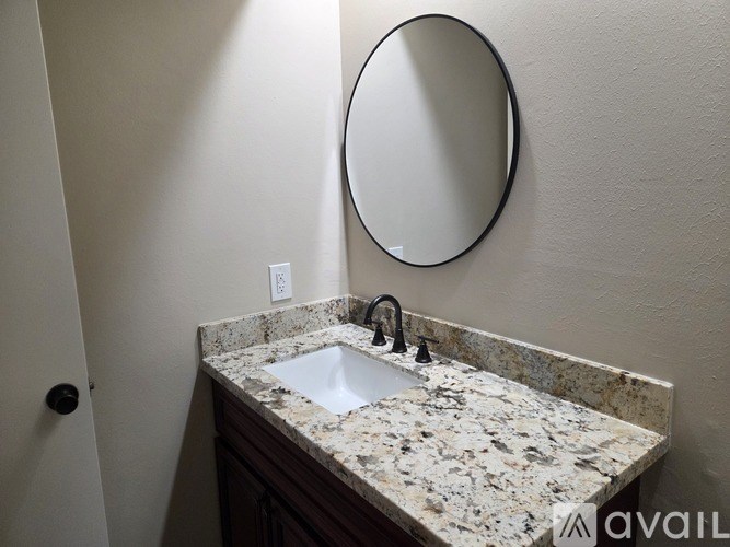 A bathroom sink with a granite countertop and a round mirror above it.