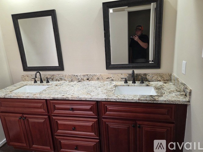A bathroom with a granite countertop and a person taking a photo in the mirror.