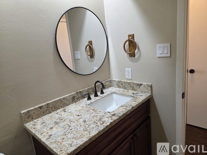 A bathroom sink with a granite countertop and a round mirror above it.