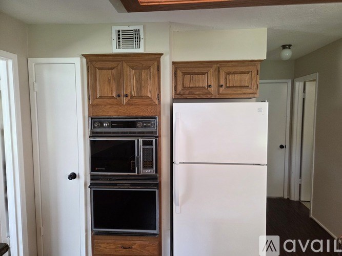 A kitchen with a white refrigerator, wooden cabinets, and a white door.