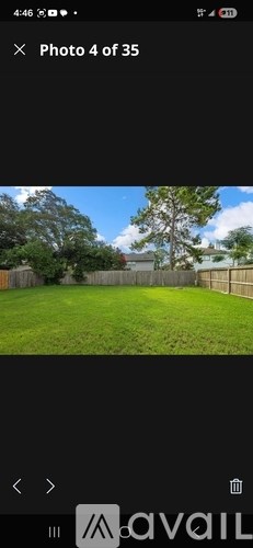 A photo of a green lawn with a fence and trees in the background.