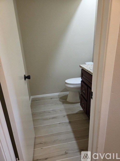 A white toilet in a small bathroom with wooden floors.