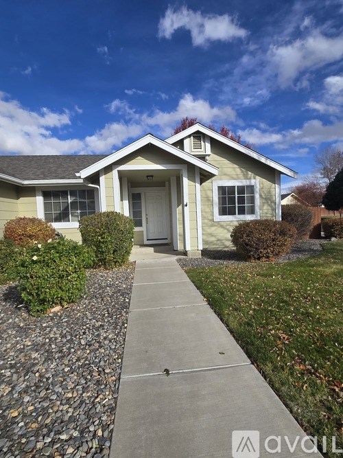 A house with a grey roof and a white door is surrounded by a gravel path.