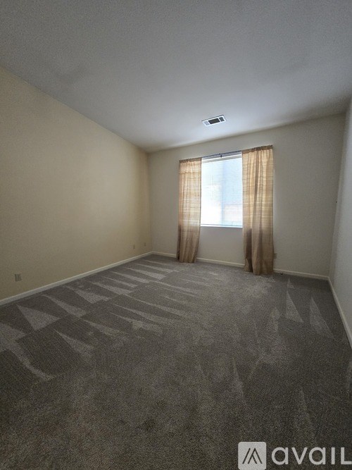 A room with a carpeted floor and a window with curtains.