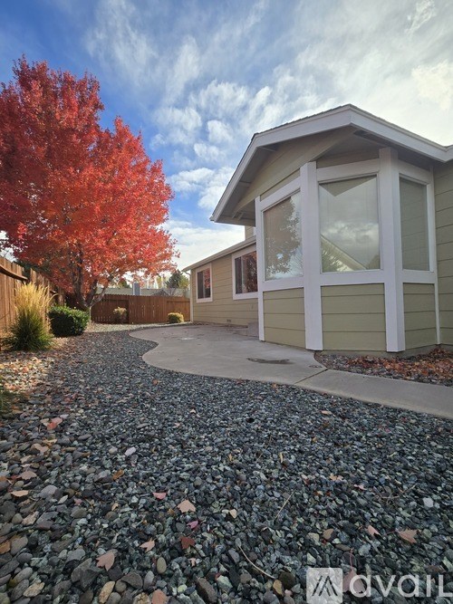 A house with a gravel driveway and a red tree in the background.