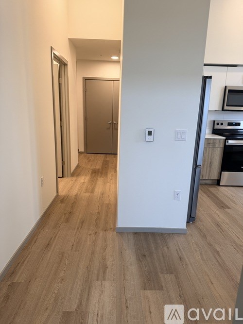 A hallway with a wooden floor and a white wall with a door on the left.