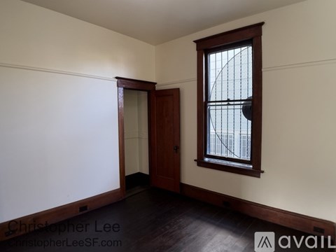 A room with a wooden floor, a window with a view of a fence, and a door.