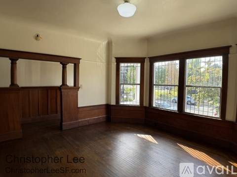 A room with wood floors and a large window with a view of trees and cars outside.